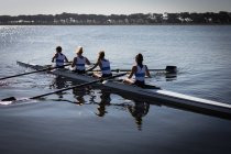 Side view of a rowing team of four Caucasian women training on the river, rowing in a racing shell in the sun — Stock Photo