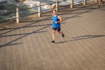 Hochwinkelfrontansicht eines älteren kaukasischen Mannes, der an einem sonnigen Tag auf einer Promenade trainiert und läuft — Stockfoto