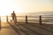 Vista lateral de um homem maduro caucasiano sênior trabalhando em um passeio em um dia ensolarado, correndo pelo mar — Fotografia de Stock