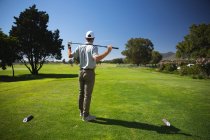 Visão traseira de um homem caucasiano em um campo de golfe em um dia ensolarado com céu azul, segurando um taco de golfe em seus ombros — Fotografia de Stock