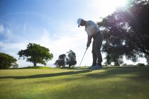 Visão lateral de baixo ângulo de um homem caucasiano em um campo de golfe em um dia ensolarado com céu azul, batendo uma bola de golfe — Fotografia de Stock