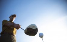Vue de face à angle bas d'un homme caucasien sur un terrain de golf par une journée ensoleillée avec un ciel bleu, se préparant à frapper une balle — Photo de stock
