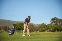 Vista frontal de un hombre caucásico en un campo de golf en un día soleado con cielo azul, preparándose para golpear una pelota - foto de stock