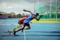 Side view of a Caucasian and a mixed race male athletes practicing at a sports stadium, starting the race from the starting blocks — Stock Photo