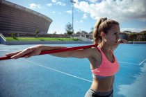 Seitenansicht einer entspannten kaukasischen Athletin, die in einem Sportstadion übt und ihre Arme auf einem über ihren Schultern liegenden Speer ruht — Stockfoto