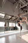 Seitenansicht einer fitten attraktiven kaukasischen Frau, die in einem Studio Pole Dance trainiert, kopfüber an der Stange hängend, mit einem Bein umschlungen und ausgestreckten Armen — Stockfoto