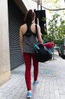 Rear view of a fit Caucasian woman walking in the street on her way to fitness training on a cloudy day, carrying a sports bag and a yoga mat — Stock Photo