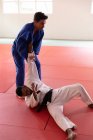 Seitenansicht eines gemischten Rennens männlicher Judo-Trainer und männlicher Judoka im Teenageralter, die blau-weiße Judogis tragen und Judo während eines Trainings in einer Sporthalle praktizieren. — Stockfoto