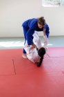 Vue de face de deux judokas adolescentes de race blanche et mixte portant des judokas bleus et blancs, pratiquant le judo lors d'un sparring dans une salle de gym. — Photo de stock