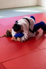 Vue latérale de deux judokas adolescentes de race blanche et mixte portant des judokas bleus et blancs, pratiquant le judo lors d'un sparring dans une salle de gym. — Photo de stock