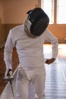 Deportista afroamericano con traje de esgrima protector durante una sesión de entrenamiento de esgrima, preparándose para un duelo, sosteniendo un pis. Esgrimistas entrenando en un gimnasio. - foto de stock