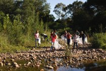 Grupo multiétnico de voluntarios de conservación limpiando el río en el campo, recogiendo basura. Ecología y responsabilidad social en el medio rural. - foto de stock