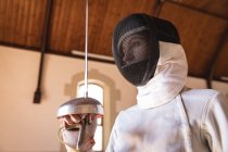Caucasian sportswoman wearing protective fencing outfit during a fencing training session, preparing for a duel, holding an epee. Fencers training at a gym. — Stock Photo