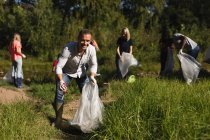 Retrato de hombres caucásicos voluntarios de conservación limpiando el río en el campo, sus amigos recogiendo basura en el fondo. Ecología y responsabilidad social en el medio rural. - foto de stock