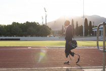 Fit, mixed race disabled male athlete at an outdoor sports stadium, walking with gym bag and water bottle on race track wearing running blades. Disability athletics sport training. — Stock Photo