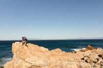 Ein fitter, behinderter Mixed Race männlicher Athlet mit Beinprothese, der seine Zeit auf einem Ausflug in die Berge, beim Wandern und Klettern auf den Felsen am Meer genießt. Aktiver Lebensstil mit Behinderung. — Stockfoto