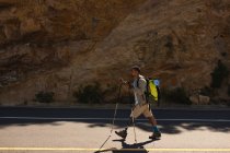A fit, disabled mixed race male athlete with prosthetic leg, enjoying his time on a trip to the mountains, hiking with sticks, walking on the road in the mountains. Active lifestyle with disability. — Stock Photo