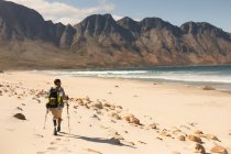 Ein fitter, behinderter Mixed-Race-Athlet mit Beinprothese, der seine Zeit bei einem Ausflug in die Berge, Wanderungen mit Stöcken und Spaziergängen am Strand am Meer genießt. Aktiver Lebensstil mit Behinderung. — Stockfoto