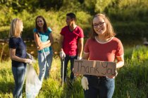 Portrait of of happy Caucasian female conservation volunteer cleaning up the countryside with board Thank You, her friends in the background. Ecology and social responsibility in rural environment. — Stock Photo