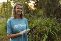Retrato de feliz caucasiana voluntária de conservação do sexo feminino limpando a floresta no campo, segurando tablet digital, sorrindo para a câmera. Ecologia e responsabilidade social no meio rural. — Fotografia de Stock