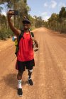 Fit, disabled mixed race male athlete with prosthetic leg, enjoying his time on a trip, hiking, standing on a dirt road in a forest, taking pictures with a smartphone. Active lifestyle with disability. — Stock Photo