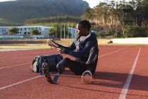In forma, atleta maschio disabile di razza mista in uno stadio sportivo all'aperto, seduto a preparare la tenuta di scarpe sportive in pista indossando lame da corsa. Disabilità atletica allenamento sportivo. — Foto stock