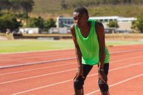 Fit, mixed race disabled male athlete at an outdoor sports stadium, on race track after race breathing and resting wearing running blades. Disability athletics sport training. — Stock Photo
