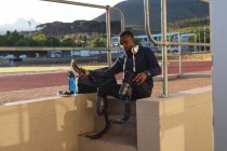 Fit, Mixed Race behinderter männlicher Athlet in einem Outdoor-Sportstadion, sitzt an der Rennstrecke und bereitet sich mit Sportschuhen und Laufschuhen vor. Behindertensport. — Stockfoto