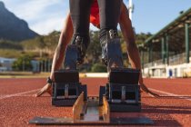 Fit disabled male athlete at an outdoor sports stadium, bending in starting blocks on race track wearing running blades. Disability athletics sport training. — Stock Photo