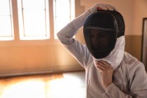 Esportista caucasiana vestindo roupa de esgrima protetora durante uma sessão de treinamento de esgrima, se preparando para um duelo, colocando máscara. Treinamento de esgrimistas em um ginásio. — Fotografia de Stock