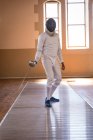 Desportista afro-americana vestindo roupa de esgrima protetora durante uma sessão de treinamento de esgrima, preparando-se para um duelo, segurando um epee. Treinamento de esgrimistas em um ginásio. — Fotografia de Stock