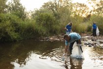 Groupe multiethnique de bénévoles de la conservation qui nettoient les rivières à la campagne, ramassent les ordures. Écologie et responsabilité sociale en milieu rural. — Photo de stock