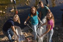 Retrato de un feliz grupo multiétnico de voluntarios de conservación limpiando el río en el campo, recogiendo basura sonriendo a la cámara. Ecología y responsabilidad social en el medio rural. - foto de stock