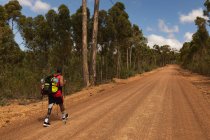 Un atleta maschio di razza mista in forma e disabile con gamba protesica, che si gode il suo tempo in viaggio, camminando, camminando con bastoni su strada sterrata in un bosco. Stile di vita attivo con disabilità. — Foto stock