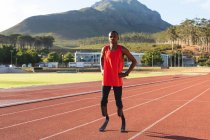 Portrait of fit, mixed race disabled male athlete at an outdoor sports stadium, standing with hands on hips on race track wearing running blades. Disability athletics sport training. — Stock Photo