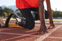 Low section of fit, disabled male athlete at an outdoor sports stadium, kneeling in starting blocks on race track wearing running blades. Disability athletics sport training. — Stock Photo