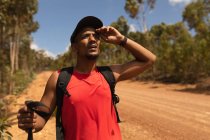 Ein fitter, behinderter Mixed-Race-Athlet mit Beinprothese, der seine Zeit beim Wandern genießt, auf einem Feldweg im Wald steht und nach vorne blickt. Aktiver Lebensstil mit Behinderung. — Stockfoto