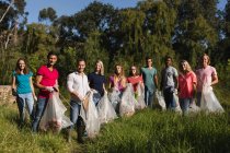 Retrato de un feliz grupo multiétnico de voluntarios de conservación limpiando el río en el campo, sosteniendo bolsas de basura. Ecología y responsabilidad social en el medio rural. - foto de stock