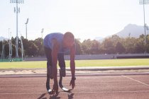 Fit, mixed race disabled male athlete at an outdoor sports stadium, preparing before workout stretching on race track wearing running blades. Disability athletics sport training. — Stock Photo