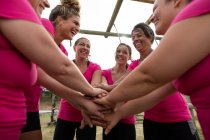 Grupo multi-étnico de mulheres todas vestindo camisetas rosa em uma sessão de treinamento de campo de treinamento, exercitando, motivando umas às outras e empilhando as mãos. Exercício de grupo ao ar livre, desafio saudável divertido. — Fotografia de Stock