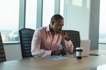 Афроамериканский бизнесмен, работающий допоздна в современном офисе, сидящий за столом и пользующийся ноутбуком. — стоковое фото