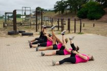 Multi-ethnische Gruppe von Frauen, alle tragen pinkfarbene T-Shirts bei einem Bootcamp-Training, machen Sport, strecken ihre Beine, liegen auf dem Boden. Bewegung in der Gruppe, Spaß und gesunde Herausforderung. — Stockfoto