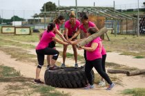 Grupo multi-étnico de mulheres todas vestindo camisetas cor-de-rosa em uma sessão de treinamento de campo de treinamento, exercitando mãos motivadoras e empilhadas. Exercício de grupo ao ar livre, desafio saudável divertido. — Fotografia de Stock