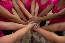 Groupe de femmes qui portent toutes des t-shirts roses lors d'une séance d'entraînement au camp d'entraînement, de l'exercice, de la motivation et de l'empilement des mains. Exercice de groupe en plein air, défi sain amusant. — Photo de stock