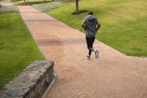 Disabled mixed race man with a prosthetic leg, working out in an urban park, wearing hooded top running on a path. Fitness disability healthy lifestyle. — Stock Photo
