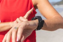 Close up of woman enjoying exercising on a beach on a sunny day, standing and using her smartwatch with sea in the background. — Stock Photo