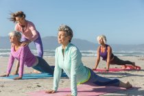 Gruppo di amiche caucasiche che si esercitano su una spiaggia in una giornata di sole, praticano yoga e si allungano in posizione yoga. — Foto stock
