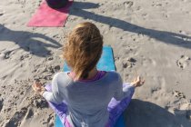 Groupe d'amies caucasiennes profitant de l'exercice sur une plage par une journée ensoleillée, pratiquant le yoga, s'asseyant et méditant en position lotus. — Photo de stock