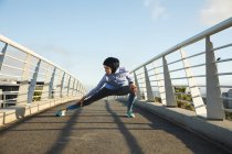 Fit gemischte Rennläuferin in Hijab und Sportbekleidung, die an einem sonnigen Tag im Freien in der Stadt trainiert und ihre Beine auf einer Fußgängerbrücke streckt. Bewegung im städtischen Lebensstil. — Stockfoto