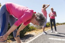 Groupe d'amies caucasiennes qui aiment faire de l'exercice par une journée ensoleillée, faire une pause après la course à pied, porter des chiffres et des vêtements de sport roses. — Photo de stock